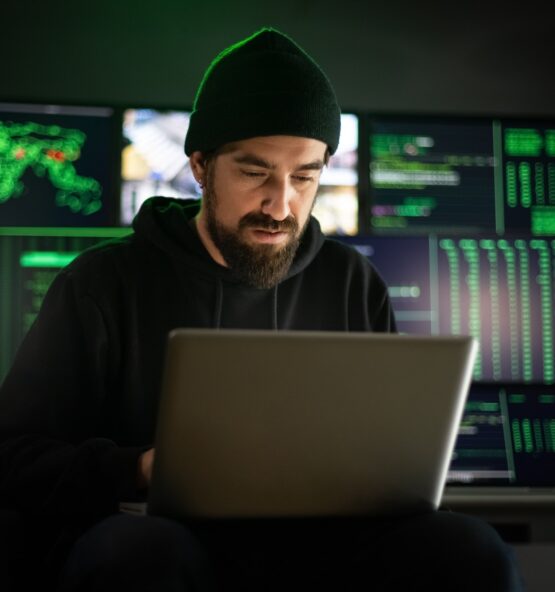 Hacker masculino caucasiano usando laptop para organizar ataques de malware em escala global.