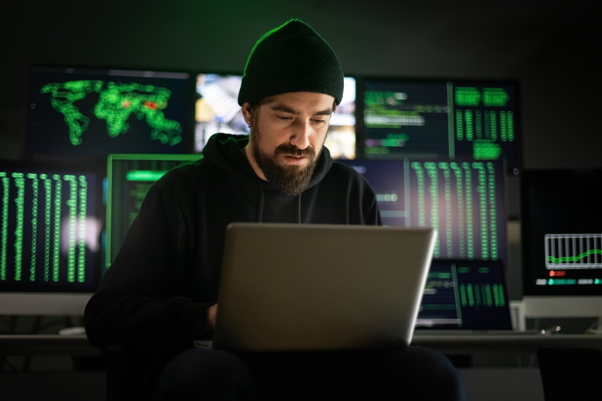 Hacker masculino caucasiano usando laptop para organizar ataques de malware em escala global.